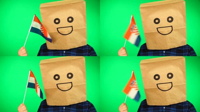 男子的肖像，头上戴着纸袋，在绿色的背景下挥舞着克罗地亚国旗，面带微笑。
