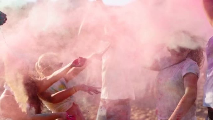 欢快的人玩得开心，在海滩上慢动作飞溅彩色粉末庆祝胡里节。朋友跳舞，跳上印度教的春天节，颜色，爱。co