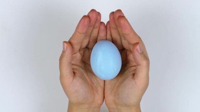 女人手里拿着一个蓝色的鸡蛋，用手掌盖住它。从她双手上方看的景色。复活节的概念，为假期做准备。