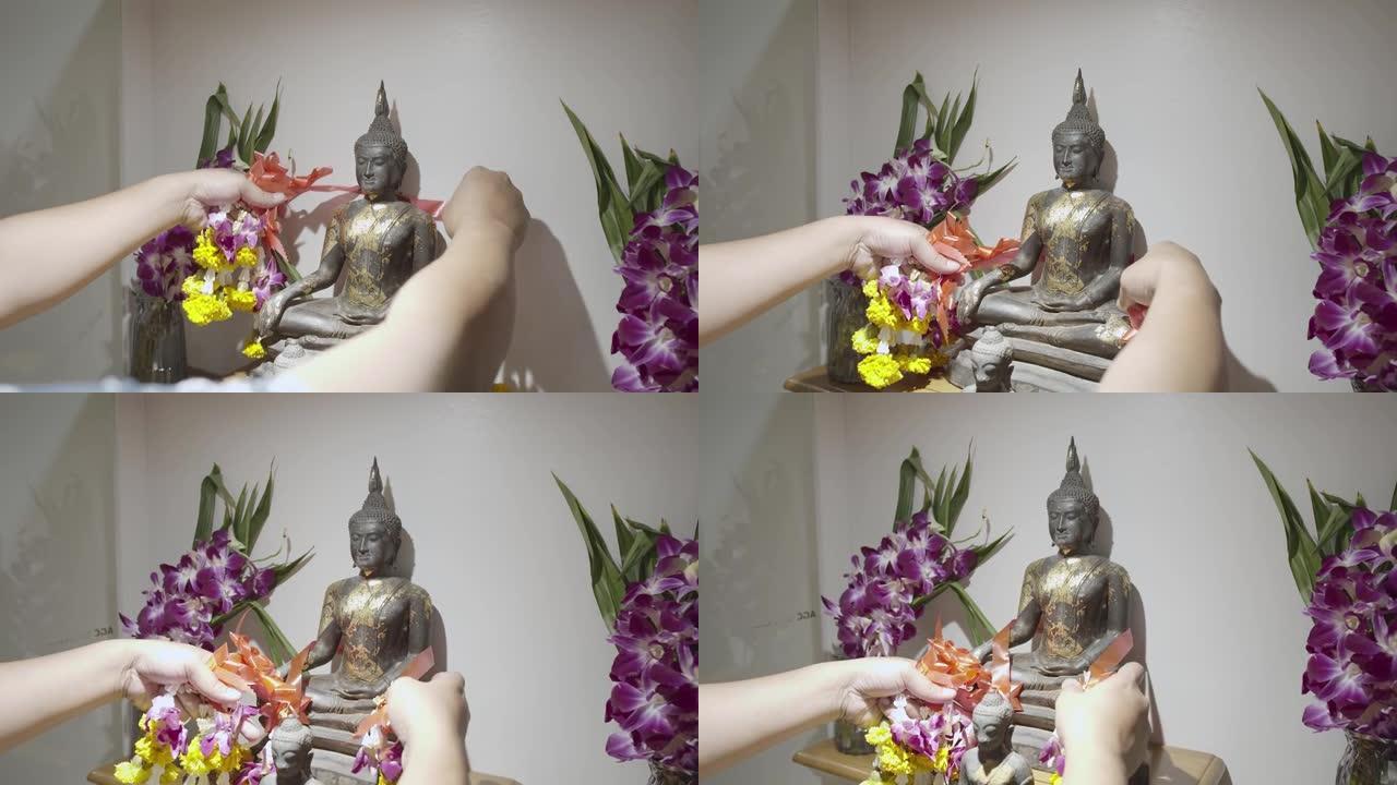 人的手拿着漂亮的花装饰在家里的佛像上