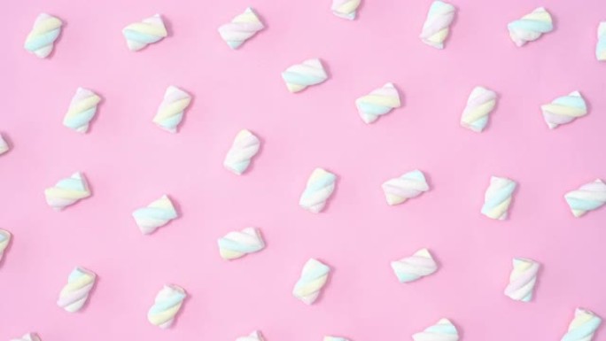 创意甜美的图案，棉花糖糖果在柔和的粉红色背景上移动。停止运动平铺