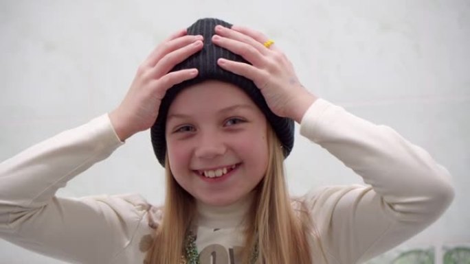 开朗的微笑女孩一边看镜头，一边调整冬天的帽子。