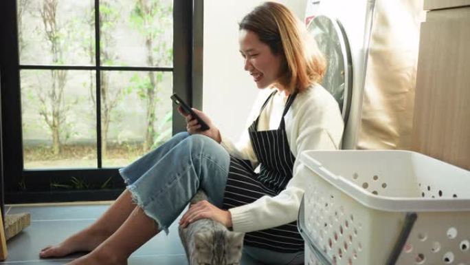 清洁社交媒体网络和技术生活方式概念后，年轻的亚洲女性在家里的多功能厅内使用智能手机在休息时慢动作场景