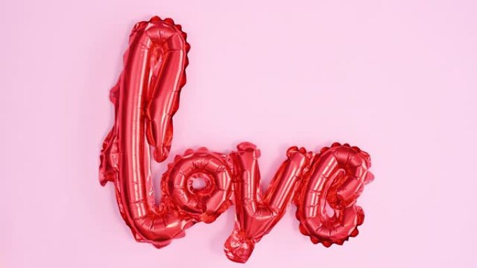 在柔和的粉红色主题上吹红色爱情文字气球。情人节停止运动