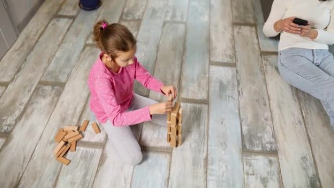 无所谓的母亲用手机，女儿在家里的地板上玩木结构
