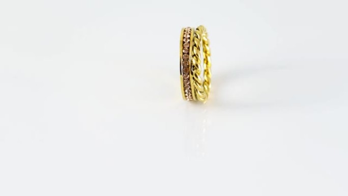 旋转金色打结闪闪发光的双金戒指，白色背景上有锆石。美丽的情人节礼物。