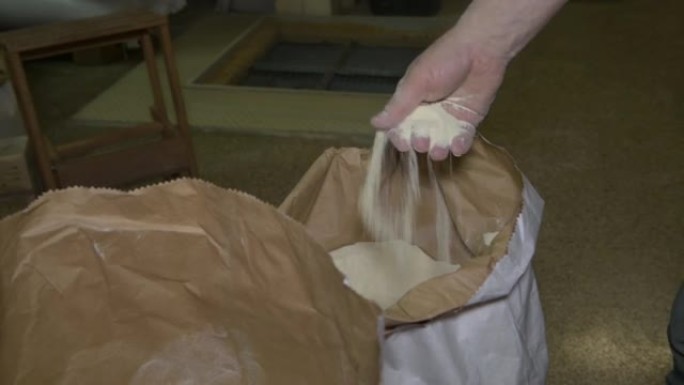 一只雄性的手碰到麻袋里的全麦面粉，从手上倒面粉