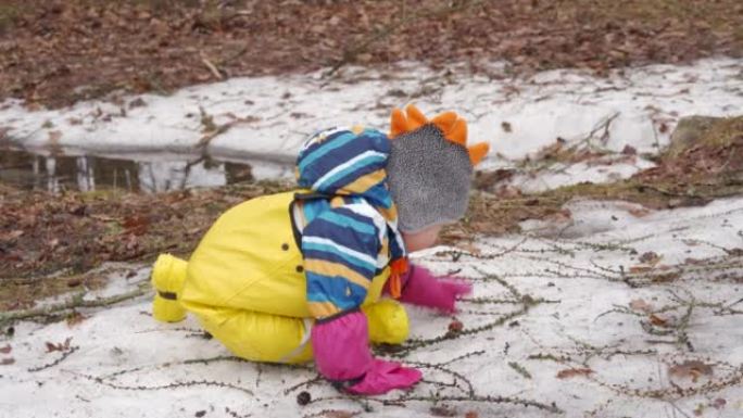 黄色防水雨裤围兜的孩子在寒冷的季节散步，一岁的男婴在阳光明媚的冬日在雪地里玩耍。