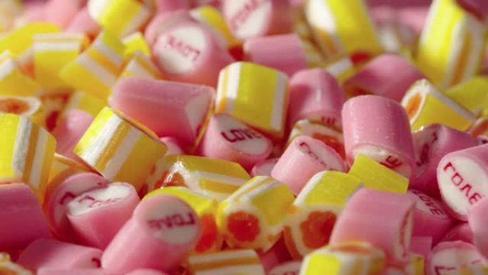 彩色条纹焦糖糖果与铭文爱，旋转镜头。粉色和黄色棒棒糖的混合特写。甜糖甜点。糖果店。节日或儿童生日的节