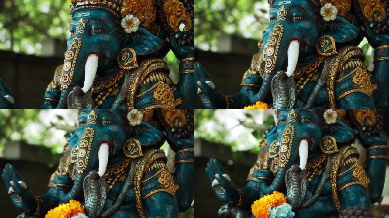 盖尼萨 (Ganesha) 的古老石像，长满苔藓，脖子上有黄色的花环，站在绿色植物的街道上