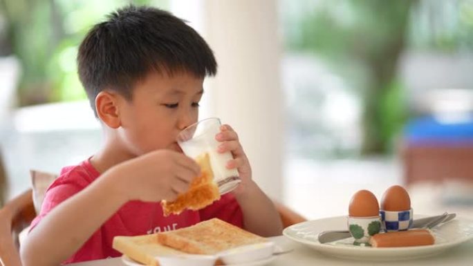 亚洲孩子早餐喝一杯牛奶。健康早餐的概念