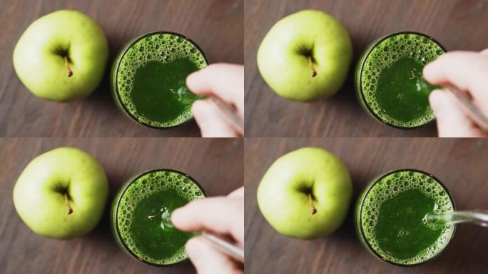 美味的绿色冰沙在玻璃杯中，与饮料吸管混合，木制背景，俯视图。健康饮食的概念。