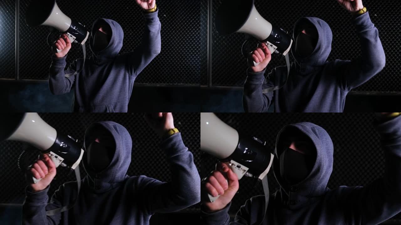 一名戴着兜帽和黑色面罩的男性活动人士对着扩音器喊着口号，并握手。抗议。起义，集会，推翻权力，捍卫权利
