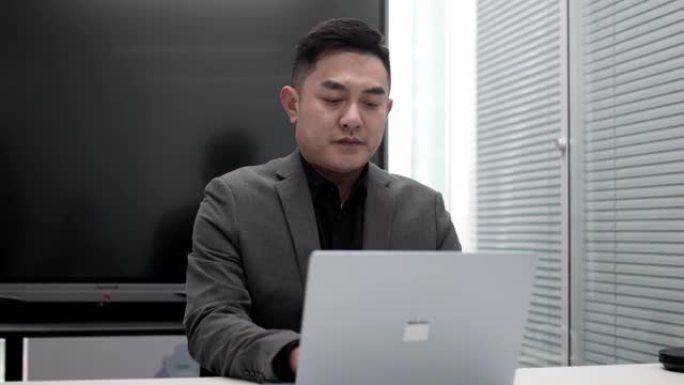 亚洲中国成熟商人，胡须打字并回复电子邮件给客户，并在办公室使用笔记本电脑与客户进行视频通话