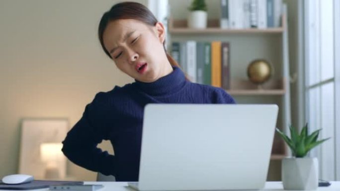 疲倦的年轻亚洲妇女在努力工作笔记本电脑时腰酸背痛，办公室综合症