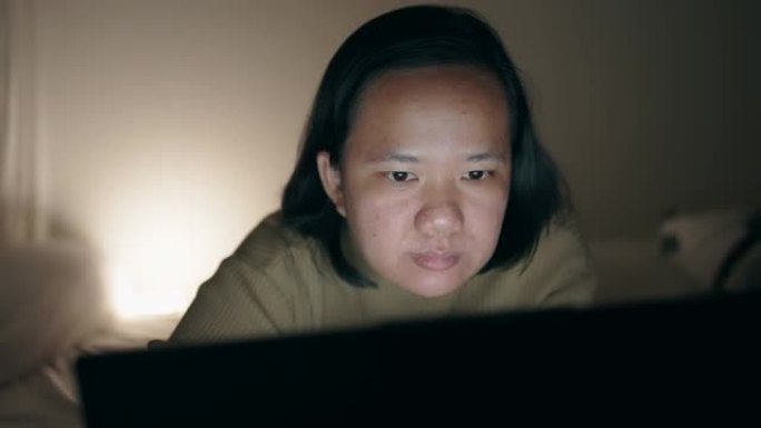 亚洲女子晚上躺在床上用笔记本电脑看电影
