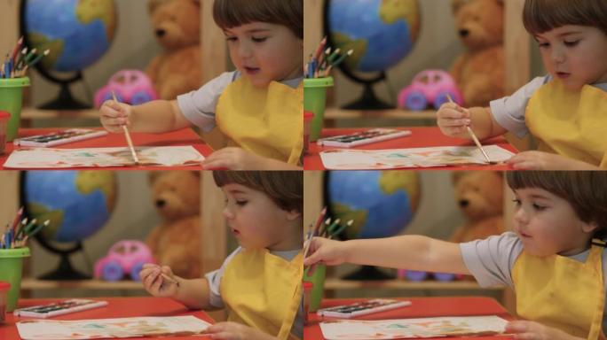 可爱的小男孩坐着画画。四岁的高加索男孩玩得开心，在纸上画画，富有创造性和艺术性。用彩色颜料在纸上特写