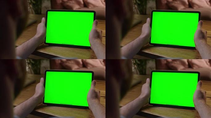手持相机: 肩膀上的年轻人在家中使用绿色模拟屏幕平板电脑。无需触摸小工具屏幕即可观看内容。浏览互联网