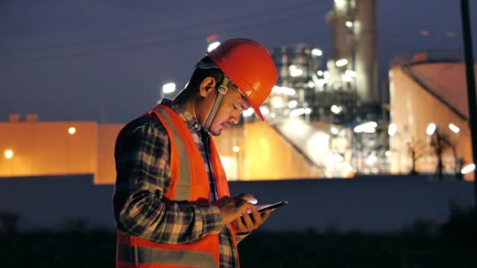 工程师在晚上在发电厂附近使用智能手机。