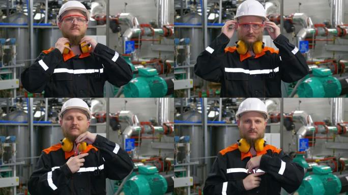一位戴着白色头盔的大胡子工业工程师站在生产车间的工作场所，脱下防护耳机和护目镜。重工业工人看着镜头
