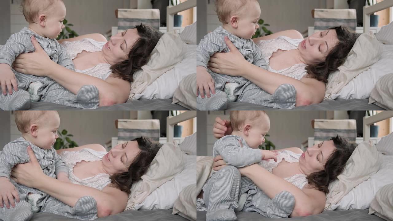 一位穿着睡衣的白人黑发母亲和她的小新生儿一起醒来，在床上放松。带着婴儿睡在家里的年轻女子。同床概念。