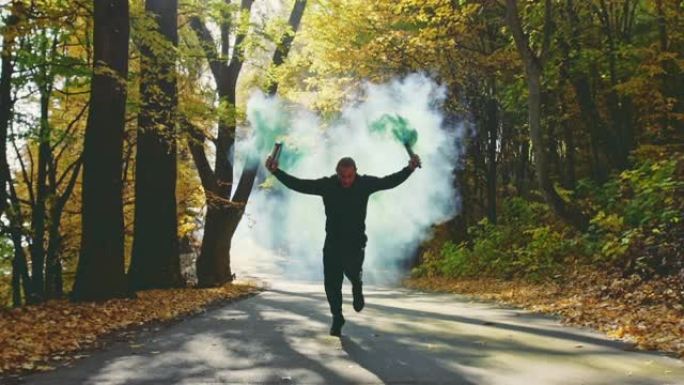 健康的运动员沿着森林道路奔跑，五颜六色的秋叶举着高空燃烧的耀斑拖着烟雾