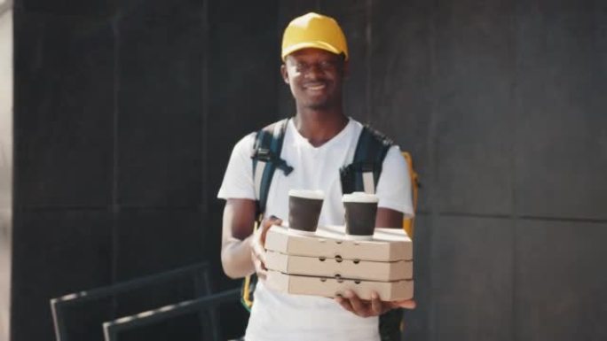 年轻的非洲送货员穿着白色制服，带着披萨盒，午餐盒和咖啡，看着相机微笑，准备为客户服务。送货服务，外卖