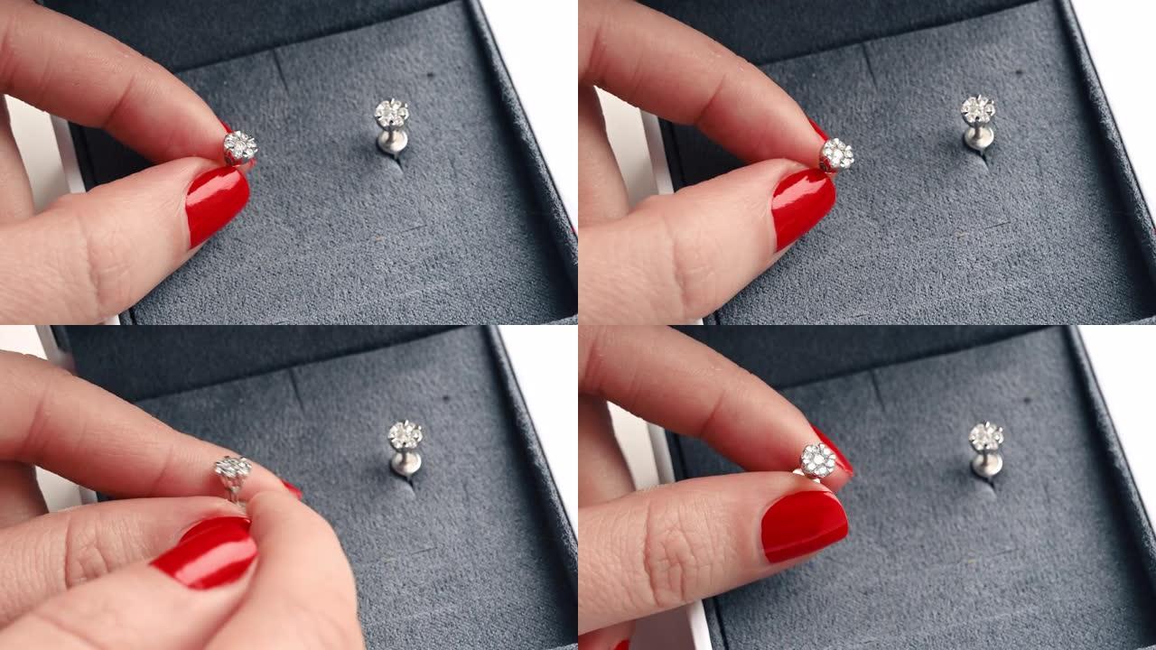 一个拿着钻石耳环的女人的近距离观察。一个装有另一个耳环的盒子，带有红色指甲的手