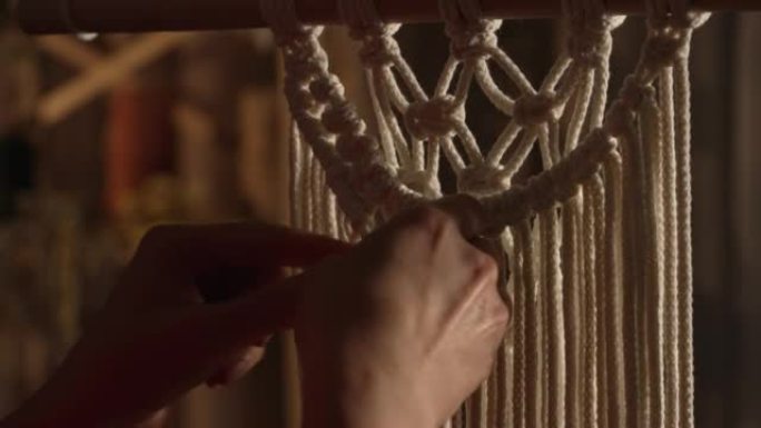 女人的手编织波西米亚风格的花边。女人在棉线上打结以创造花边。创意工作室。现代针织自然装饰理念。绳索工