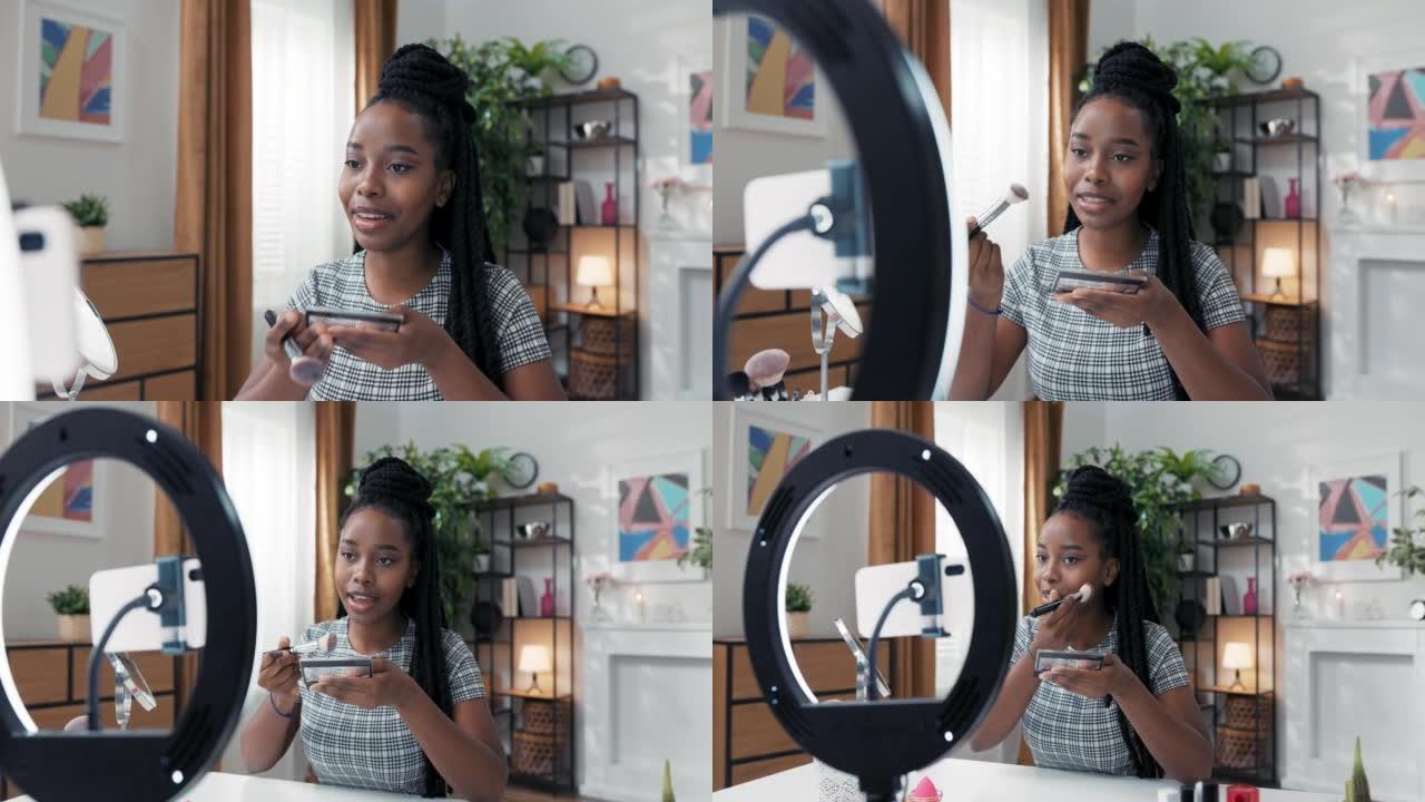 一个女孩用手机三脚架用环形灯拍摄视频。化妆师创建了有关如何正确塑造脸部轮廓的教程，她使用刷子将bro