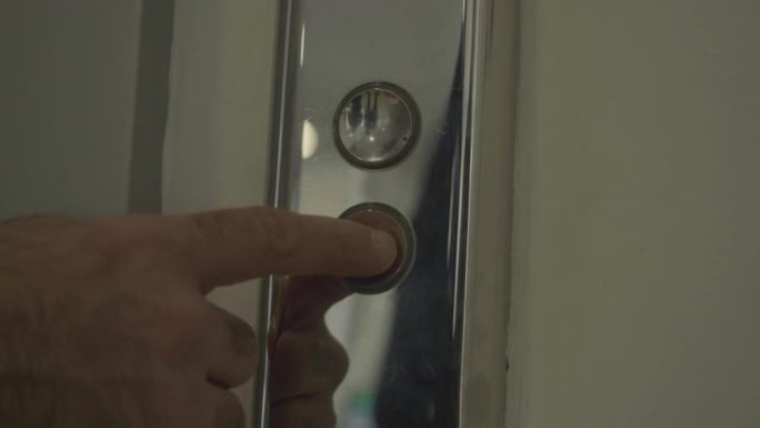 男人的手按下电梯下按钮。HDR。按下银色金属按钮，男性手指进入电梯。