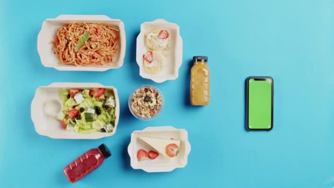 食品配送应用程序顶视图，在蓝色背景上的一次性容器中带走餐点。午餐盒的特写镜头，包括煮熟的沙拉，意大利