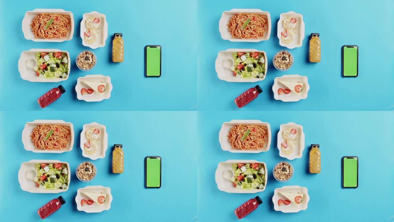 食品配送应用程序顶视图，在蓝色背景上的一次性容器中带走餐点。午餐盒的特写镜头，包括煮熟的沙拉，意大利