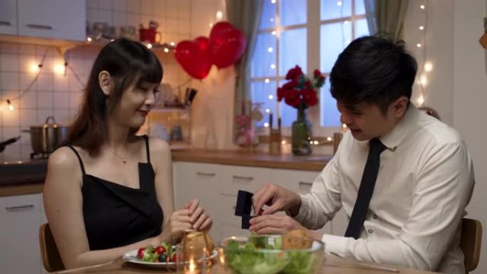 亚洲男性穿着领带和衬衫，在情人节晚宴上向女友求婚，戴上惊喜订婚戒指。在她同意嫁给他后，男人为她戴上戒