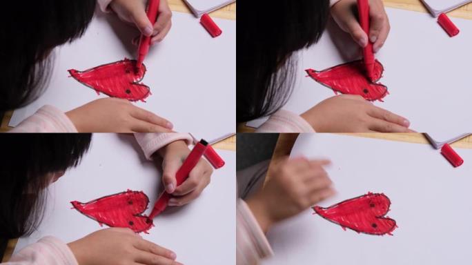 一个小女孩画一颗心并用彩色标记着色的特写镜头。可爱的年轻女孩在家桌旁做作业。工艺美术。