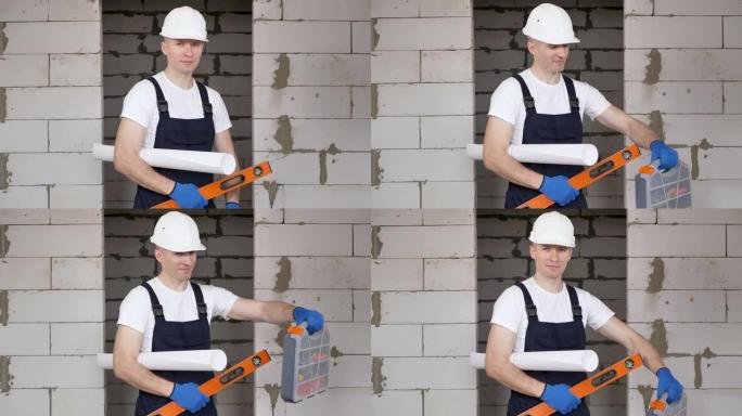 男性工人或建筑工人戴着头盔，头盔上有水平仪，工具箱，蓝图靠在砖墙上