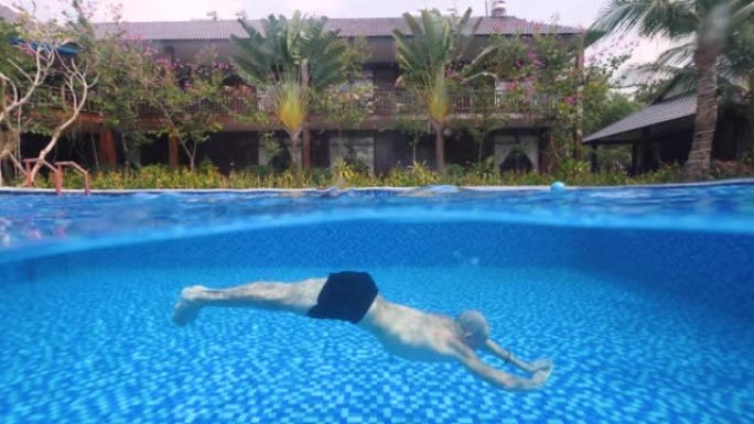 一个男人在度假胜地的夏日在游泳池里游泳的水下照片。
