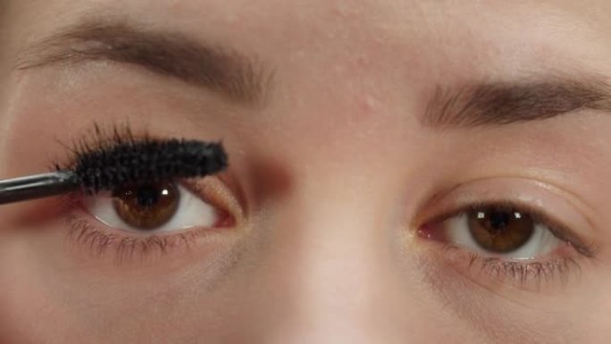 年轻女子用黑色睫毛膏睫毛刷和眨眼画睫毛的特写镜头。棕色眼睛的女孩化妆。美容和美容概念