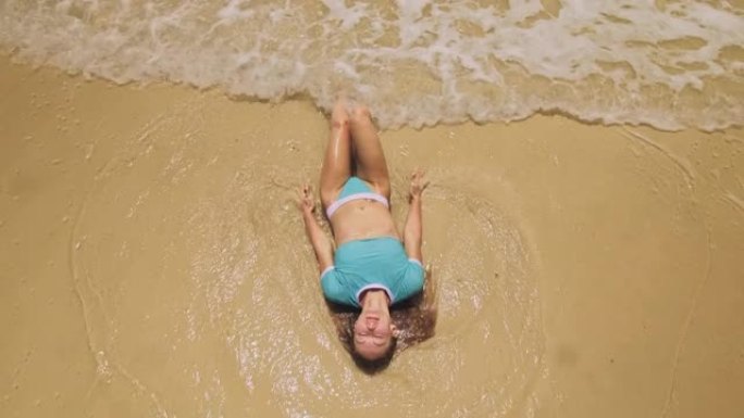 女人躺在浅水大海上。一个醉醺醺的女人正在热带岛屿上享受她的假期。女孩有趣摆姿势。俯视图