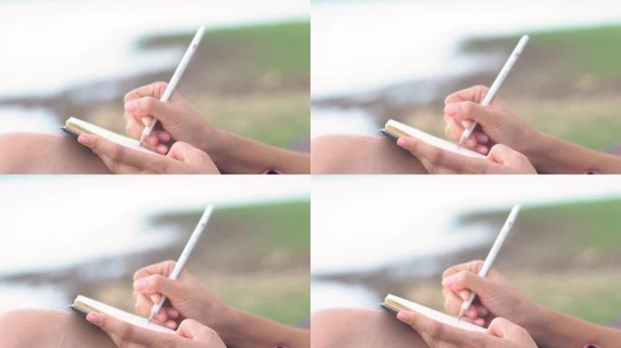 亚洲女性在户外用铅笔在笔记本上书写。