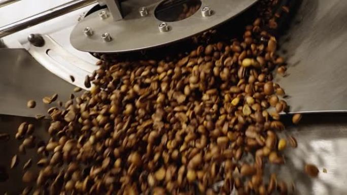 将咖啡豆倒入工厂的工业咖啡烘焙机中。混合烘焙咖啡豆。芳香棕豆旋转特写。咖啡馆的餐饮背景。慢动作