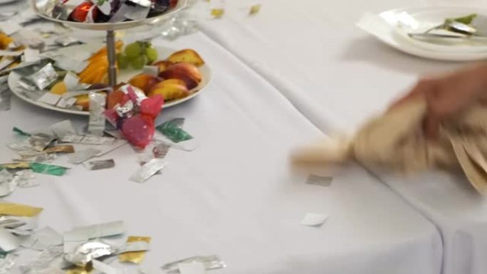 第一次婚礼舞会后，女服务员从桌子上清除了银色的五彩纸屑。有史以来最好的一天。