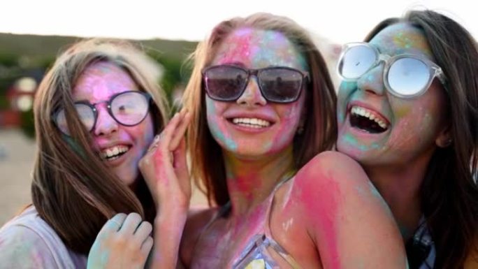 三个年轻的女人身上覆盖着五颜六色的粉末微笑，在镜头前炫耀，在慢动作特写的洒红节上玩得开心。印度教假日