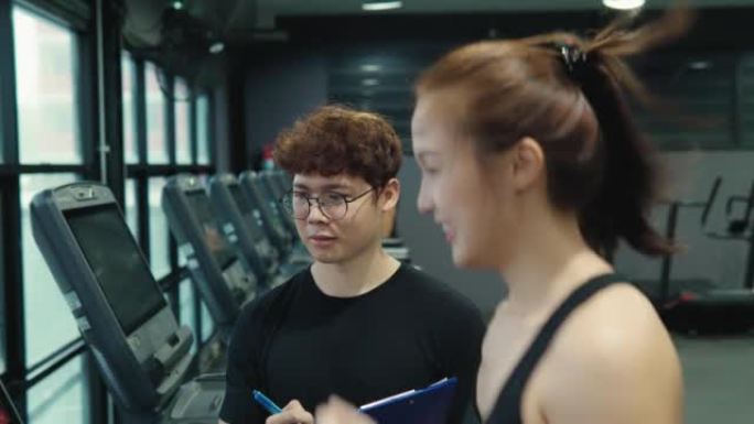 男性私人教练在健身房和一名年轻女子交谈