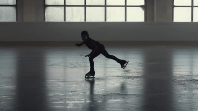 花样滑冰训练。小女孩花样滑冰运动员正在用一条腿滑冰练习旋转技巧。柔和光线的黑暗冰上舞台上的花样滑冰编