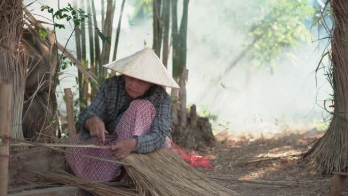 亚洲生活老奶奶在户外工作。老太太老人严重生活在泰国农村的农村。编织材料草屋顶毛边竹制。