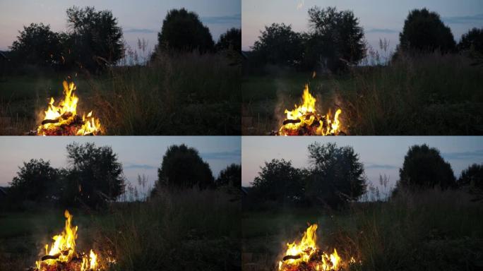 一个男人在后院的篝火里烧垃圾。报纸，旧衣服，树枝