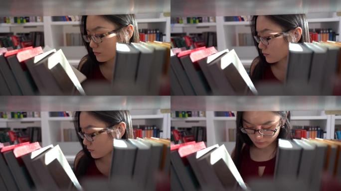 在大学图书馆学习的亚洲学生女孩。年轻女子为项目从书架上挑选书