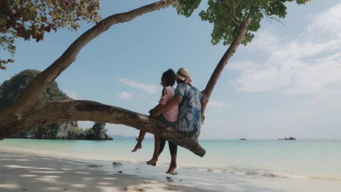 亚洲母子女孩坐在树上享受大海
