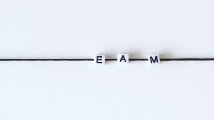 动作中的字母动画使单词 “team” 从黑色绳子上串起的印刷块中产生。白色背景。停止运动。时间流逝